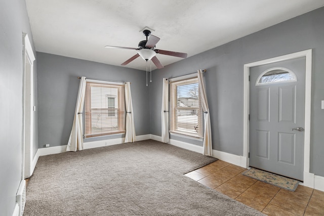 carpeted foyer entrance featuring tile patterned floors, a ceiling fan, and baseboards