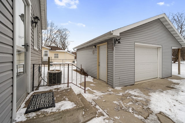 snow covered garage with a detached garage and cooling unit