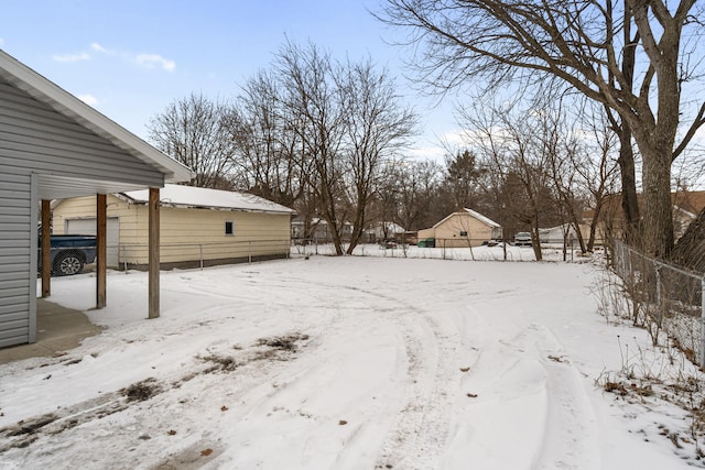 snowy yard featuring a detached garage and fence