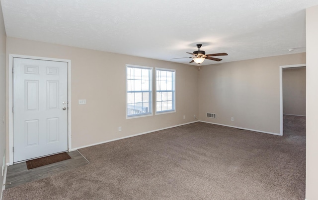 interior space with a textured ceiling, a ceiling fan, visible vents, baseboards, and dark colored carpet