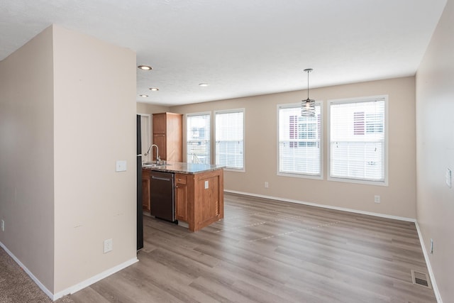 kitchen with baseboards, brown cabinetry, light wood-style flooring, pendant lighting, and stainless steel dishwasher