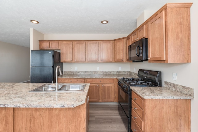 kitchen featuring black appliances, wood finished floors, a sink, and light countertops