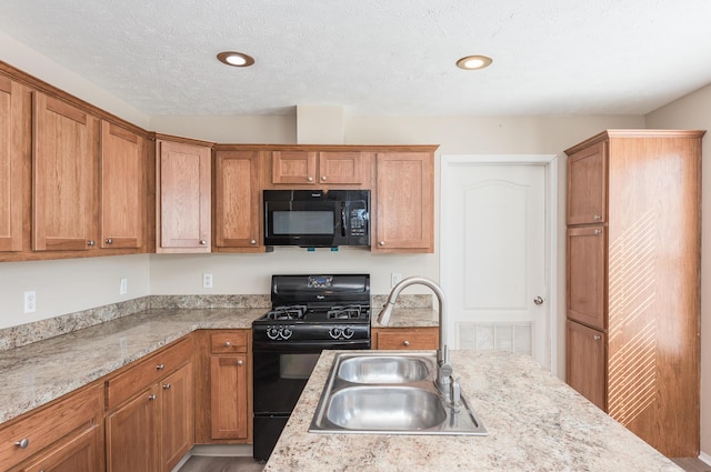 kitchen featuring a textured ceiling, a sink, visible vents, black appliances, and brown cabinetry