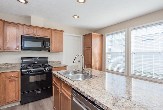 kitchen featuring recessed lighting, light wood-style flooring, brown cabinetry, a sink, and black appliances