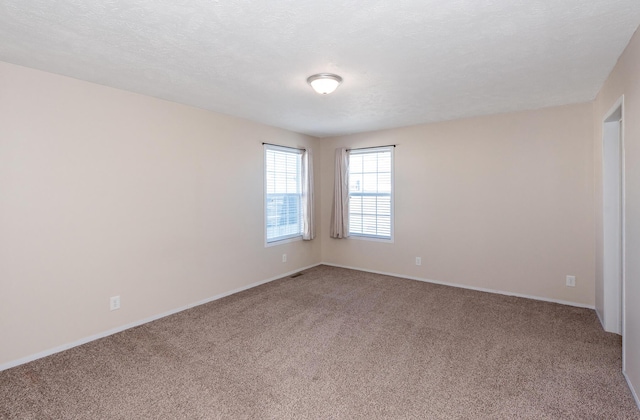 carpeted empty room with a textured ceiling and baseboards