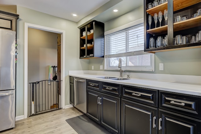 kitchen featuring dark cabinets, stainless steel appliances, light countertops, open shelves, and a sink