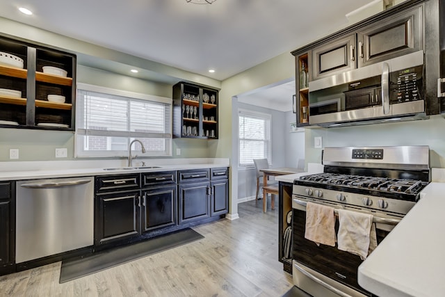 kitchen with open shelves, appliances with stainless steel finishes, a sink, and light countertops