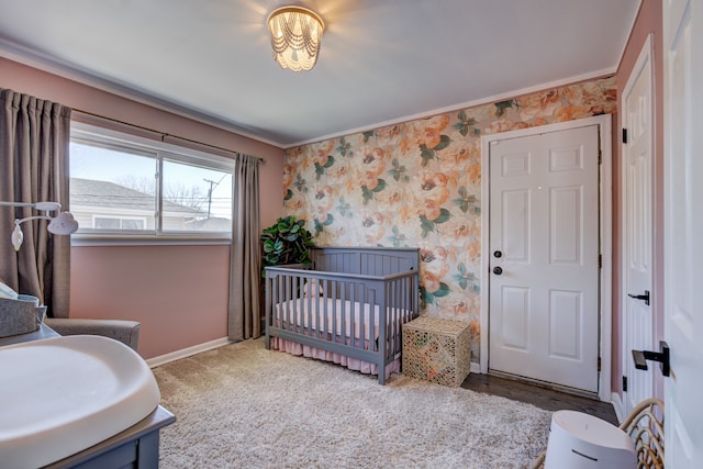 bedroom featuring baseboards, a crib, crown molding, and wallpapered walls