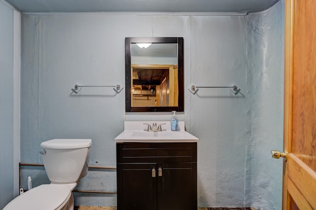 bathroom with toilet, a textured wall, and vanity