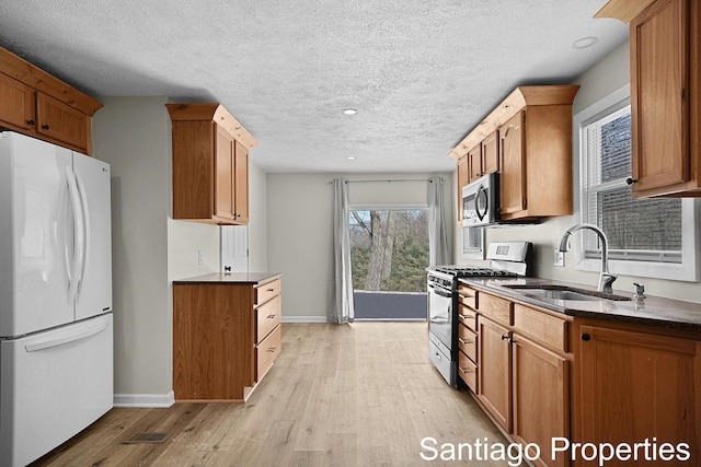 kitchen featuring stainless steel appliances, dark countertops, light wood-style floors, a sink, and baseboards