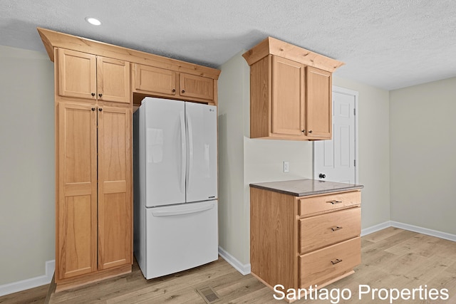 kitchen with dark countertops, light wood finished floors, light brown cabinetry, and freestanding refrigerator