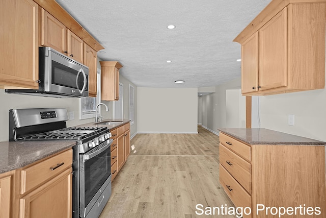 kitchen featuring stainless steel appliances, light brown cabinetry, dark stone countertops, and a sink