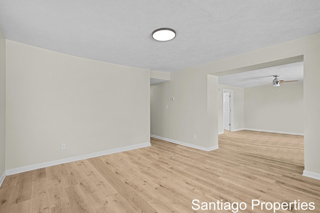 empty room with ceiling fan, light wood-style flooring, baseboards, and a textured ceiling