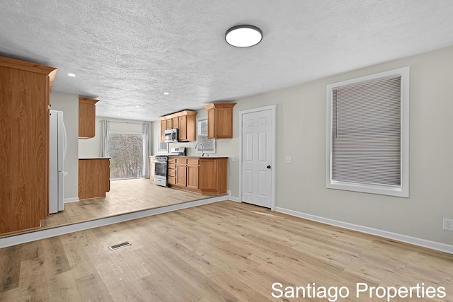 unfurnished living room with visible vents, baseboards, a textured ceiling, light wood-style floors, and a sink