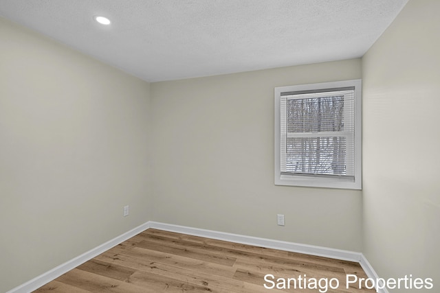 unfurnished room with a textured ceiling, light wood finished floors, and baseboards