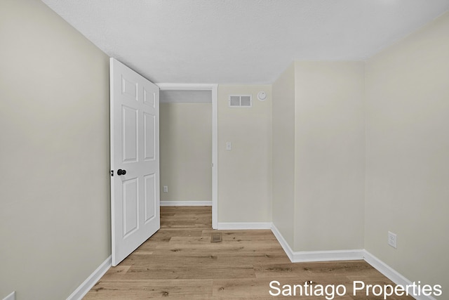 hall with light wood finished floors, visible vents, and baseboards