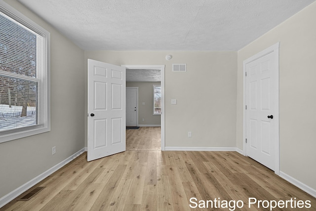 unfurnished bedroom featuring a textured ceiling, light wood finished floors, visible vents, and baseboards