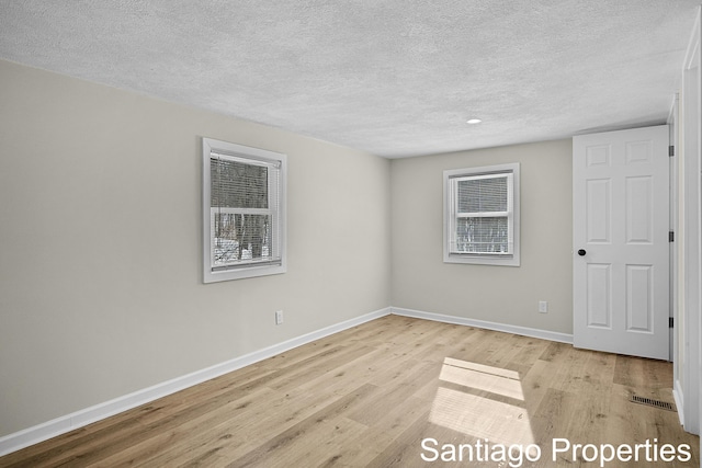 unfurnished room with a textured ceiling, light wood finished floors, visible vents, and baseboards