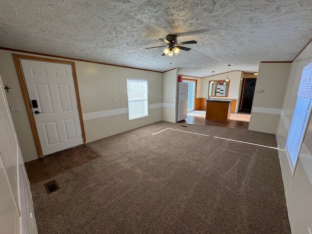 unfurnished living room featuring visible vents, vaulted ceiling, crown molding, a textured ceiling, and carpet flooring