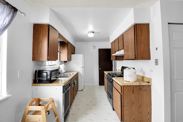 kitchen featuring light floors, light countertops, brown cabinetry, under cabinet range hood, and black appliances