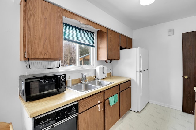 kitchen featuring freestanding refrigerator, light countertops, dishwasher, and a sink