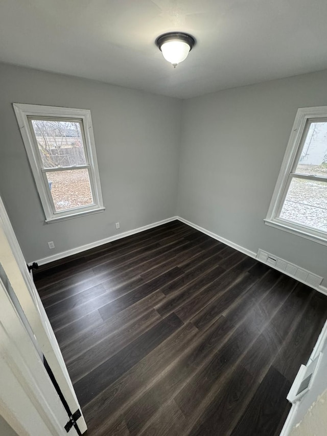 spare room with dark wood-style floors, visible vents, a wealth of natural light, and baseboards