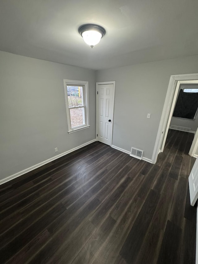 unfurnished room with dark wood-style floors, visible vents, and baseboards