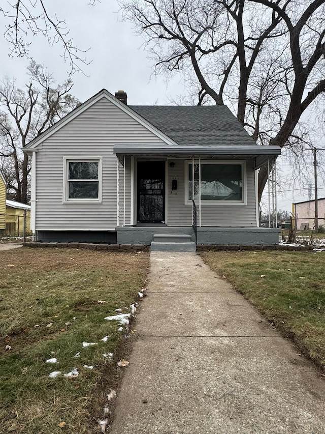 bungalow featuring covered porch, roof with shingles, a chimney, and a front yard