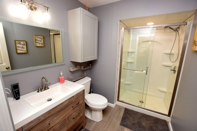 full bath with a stall shower, toilet, wood finished floors, vanity, and baseboards