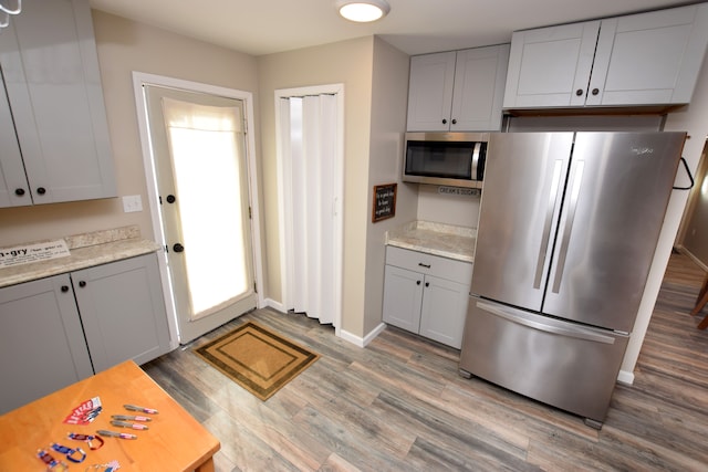 kitchen with appliances with stainless steel finishes, wood finished floors, baseboards, and gray cabinetry