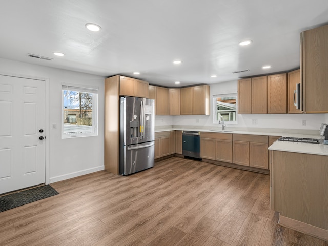 kitchen with appliances with stainless steel finishes, light wood-style flooring, a sink, and visible vents