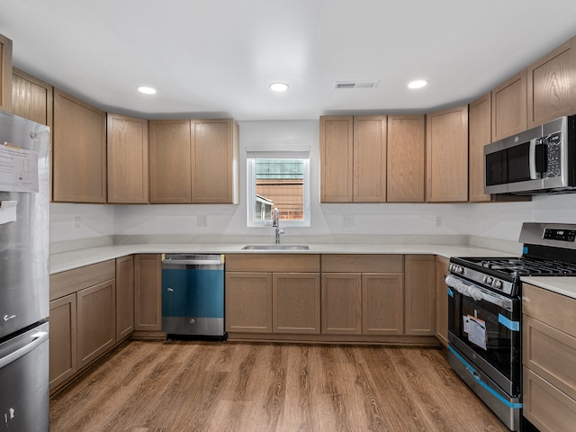 kitchen with stainless steel appliances, wood finished floors, a sink, and visible vents