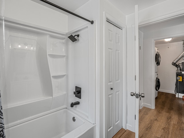 bathroom with a walk in closet, shower / washtub combination, wood finished floors, and stacked washer and clothes dryer