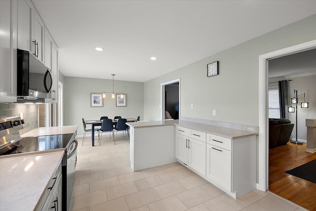 kitchen with a peninsula, stainless steel electric range, light countertops, and backsplash