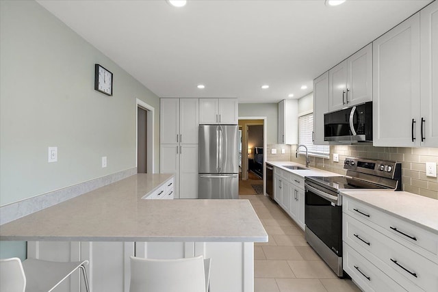 kitchen featuring decorative backsplash, a peninsula, stainless steel appliances, light countertops, and a sink