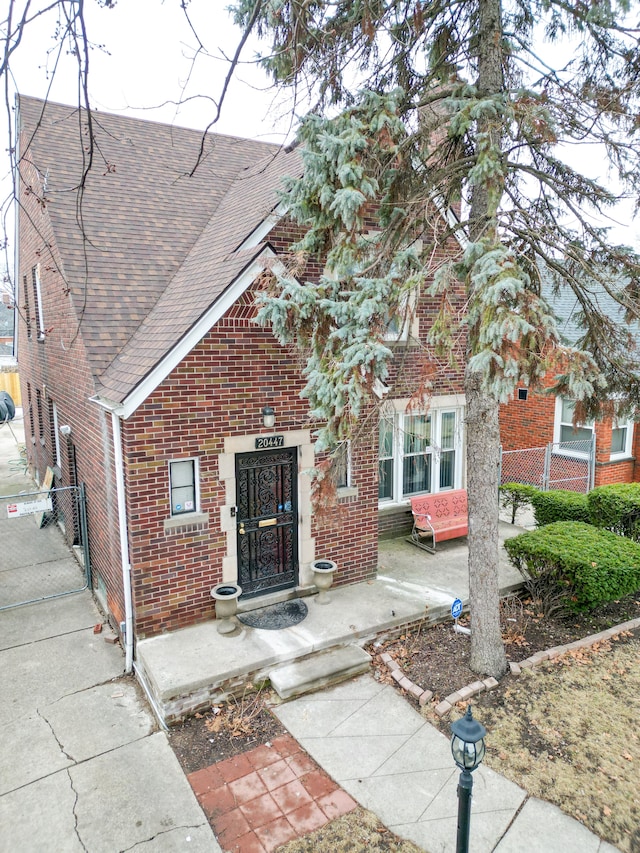 view of front facade with a shingled roof, a gate, and brick siding