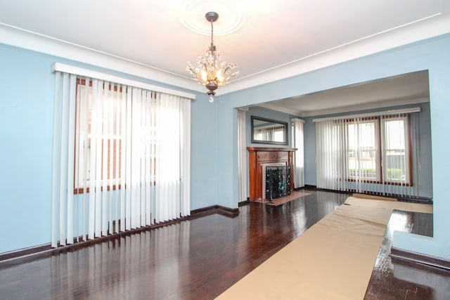 unfurnished living room featuring a chandelier, a fireplace, baseboards, and wood finished floors