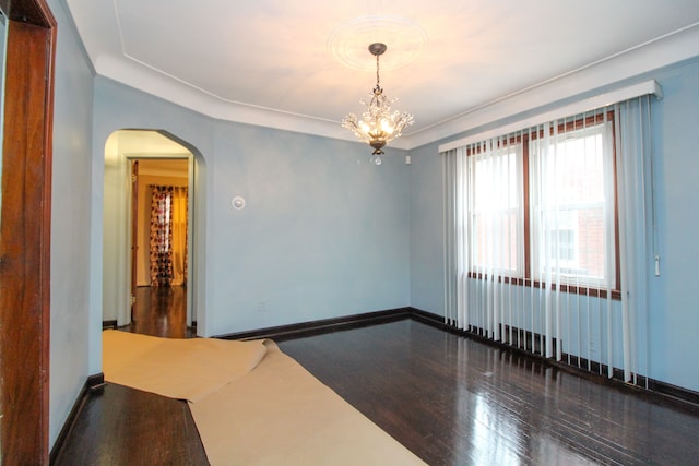 unfurnished room featuring arched walkways, an inviting chandelier, baseboards, and wood finished floors