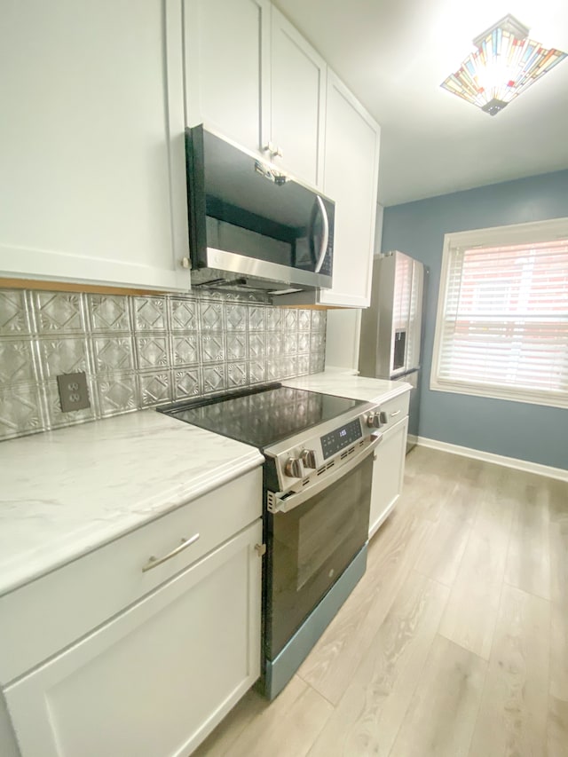 kitchen with light wood-type flooring, tasteful backsplash, white cabinets, and stainless steel appliances