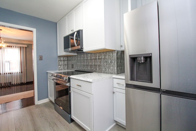 kitchen with decorative backsplash, light stone counters, stainless steel appliances, light wood-type flooring, and white cabinetry