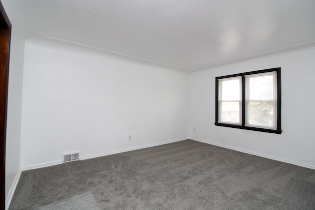 spare room featuring dark colored carpet, visible vents, and baseboards