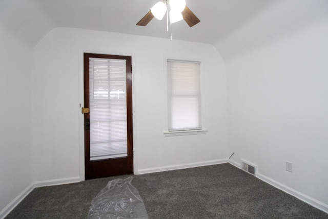 empty room featuring lofted ceiling, a healthy amount of sunlight, visible vents, and dark colored carpet