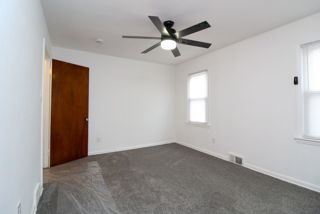 empty room with a ceiling fan, dark carpet, visible vents, and baseboards