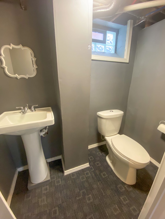 half bath with baseboards, a sink, and toilet