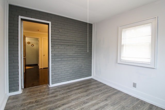 unfurnished room with baseboards, dark wood finished floors, and brick wall