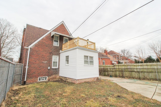 back of house featuring brick siding, a yard, a fenced backyard, and a balcony