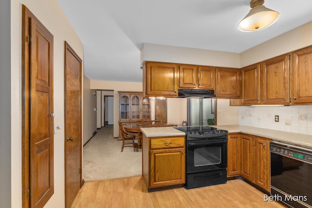 kitchen featuring brown cabinetry, under cabinet range hood, a peninsula, and black appliances