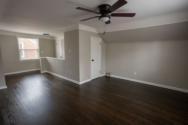 empty room with visible vents, vaulted ceiling, baseboards, and dark wood finished floors