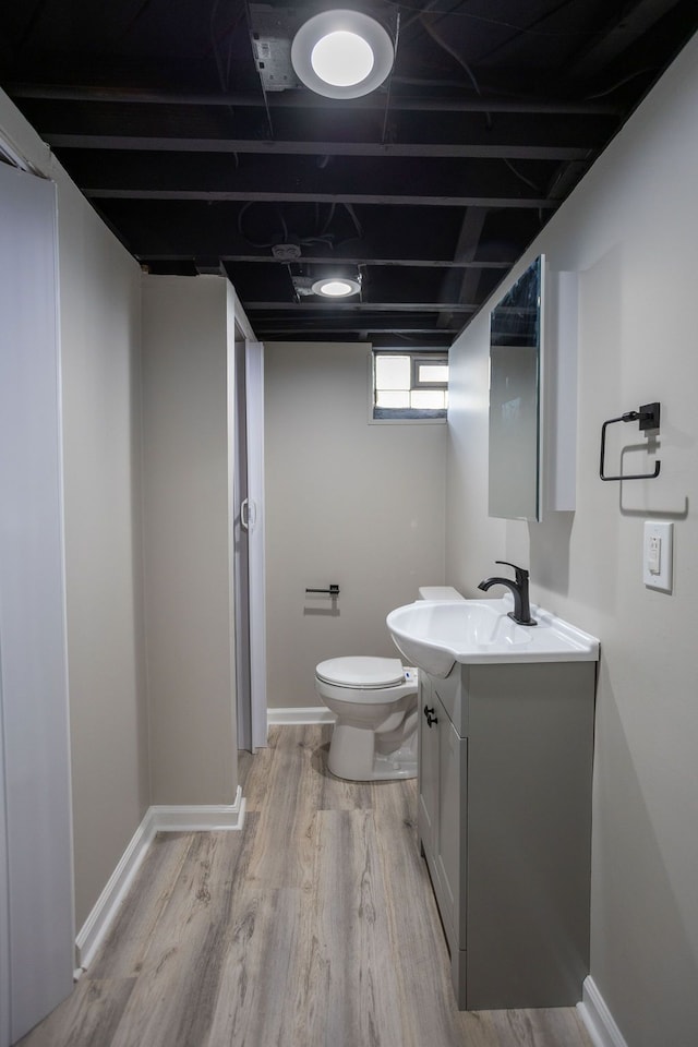 half bath featuring baseboards, vanity, toilet, and wood finished floors