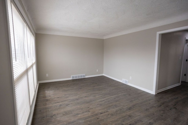 unfurnished room featuring dark wood-type flooring, visible vents, and baseboards